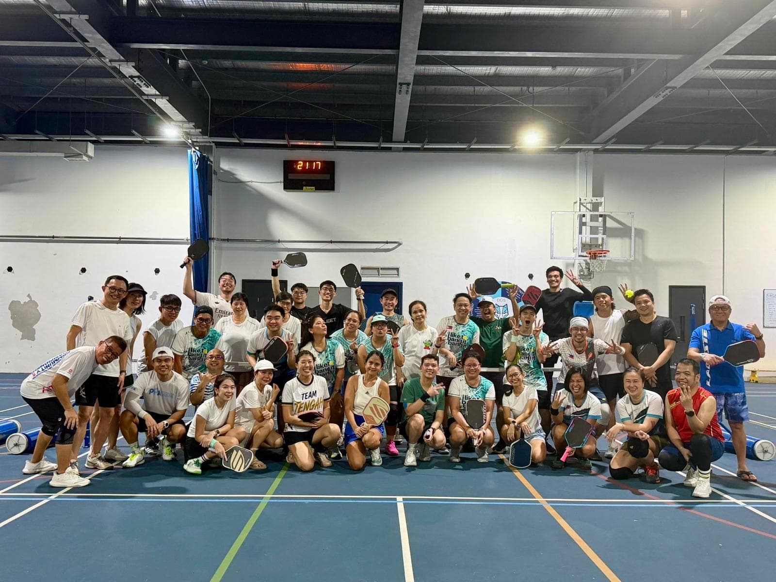 TCC and FAP players pose together for a group photo, paddles raised, in an indoor sports hall after their 29 August friendly match at Dover Court.